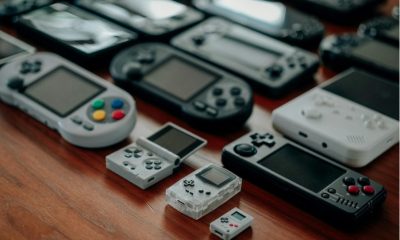 An array of retro gaming consoles is lined up on a wooden table