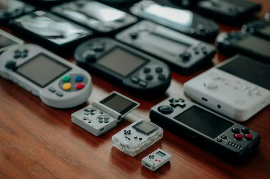 An array of retro gaming consoles is lined up on a wooden table