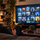 A male gamer sits on a sofa browsing a large digital game library on a TV